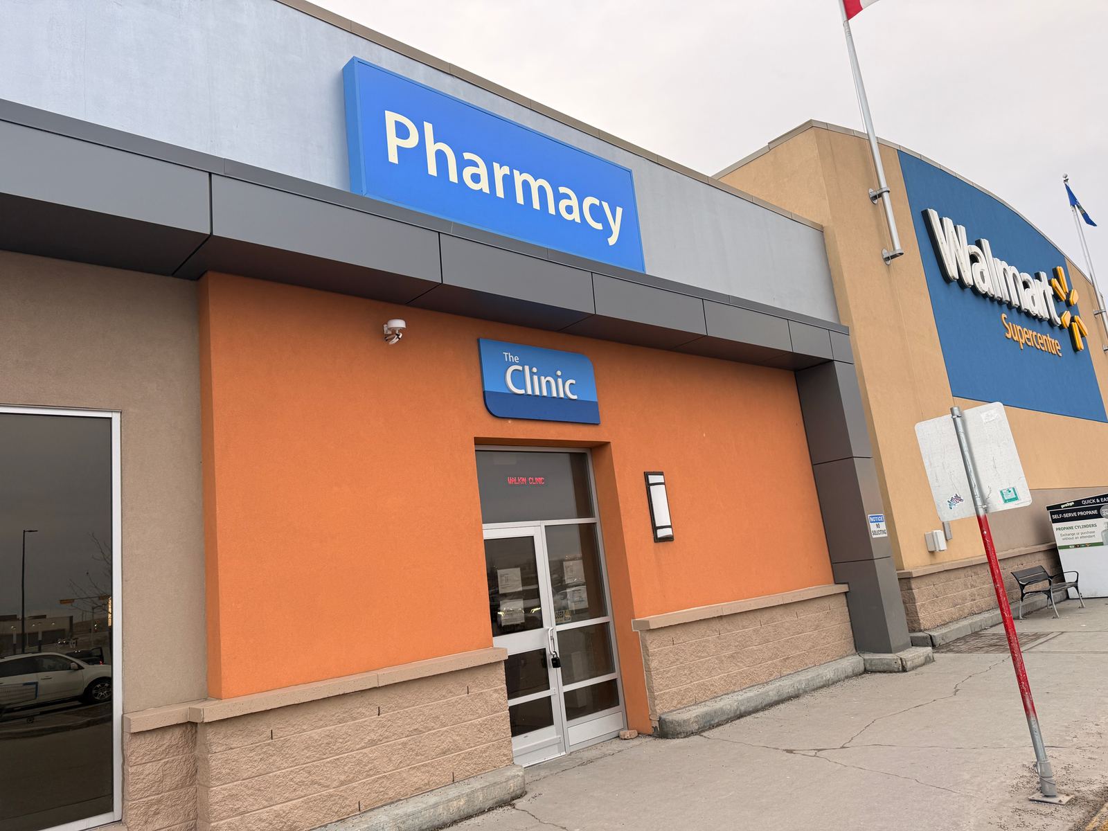 The outside of the Walmart Supercentre at East Hills, Calgary, showing the Pharmacy sign and the entrance door marked The Clinic where East Hills Medical Centre is located.